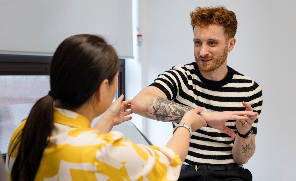 A young tattooed male with ginger hair in a black and white striped top gets his forearm looked at by a doctor