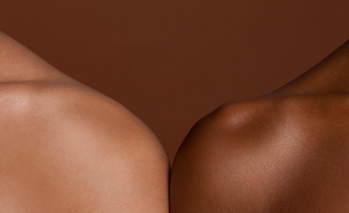 The shoulders of two women showing bare skin on a brown background