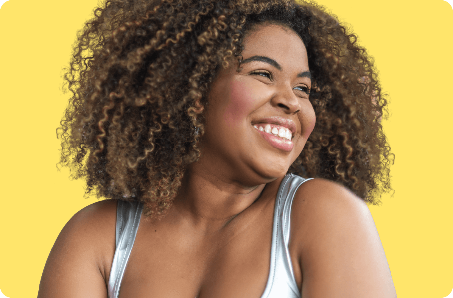 Smiling person with curly hair in a silver top against a yellow background.