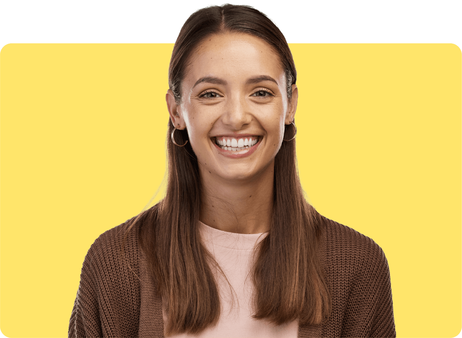 A smiling woman with long brown hair, wearing a pink shirt and brown cardigan, stands against a solid yellow background.
