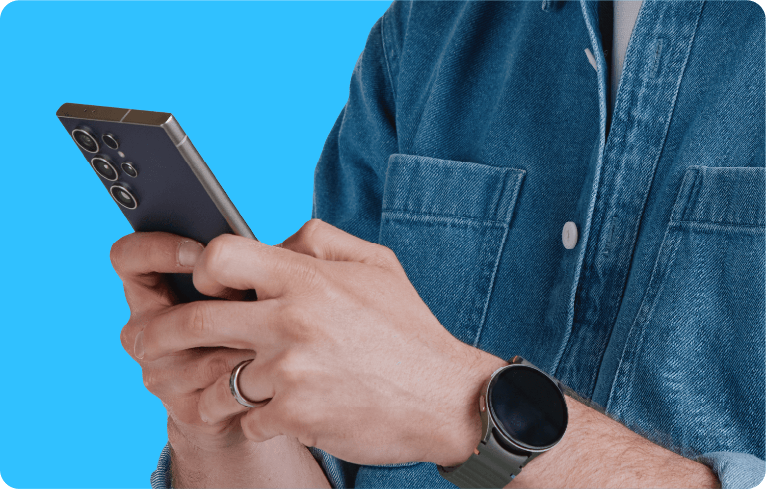 Person wearing a denim shirt and a smartwatch is holding a smartphone with multiple cameras against a blue background.