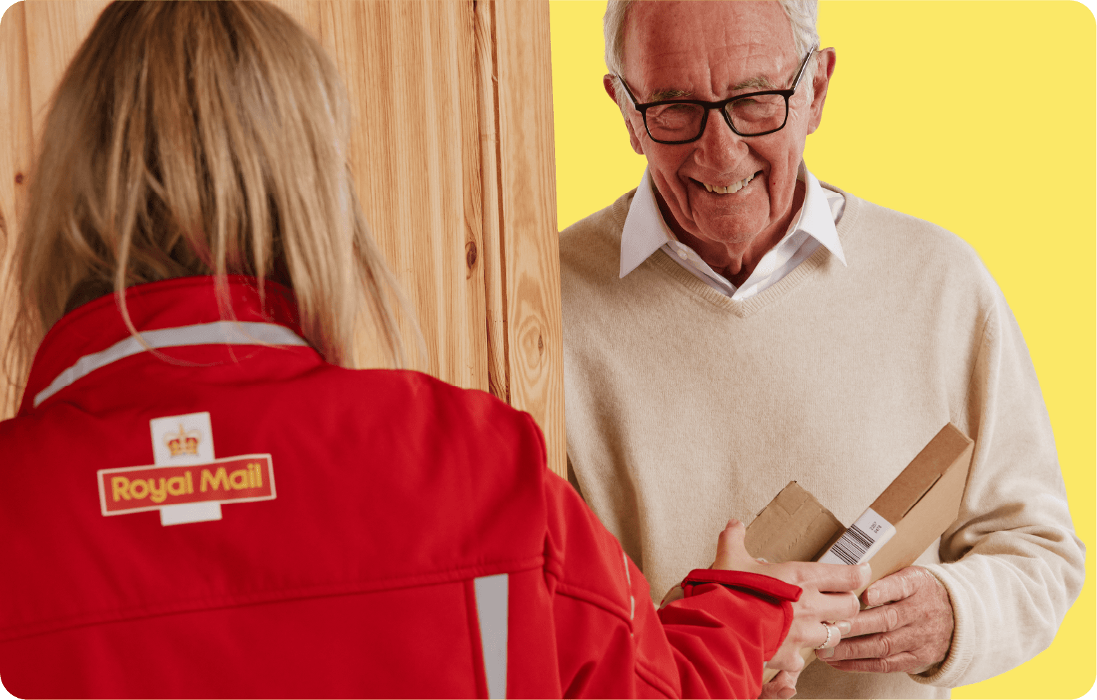 Postal worker hands a package to an elderly man at the door. He is smiling and wearing glasses, while she is in a red Royal Mail uniform.