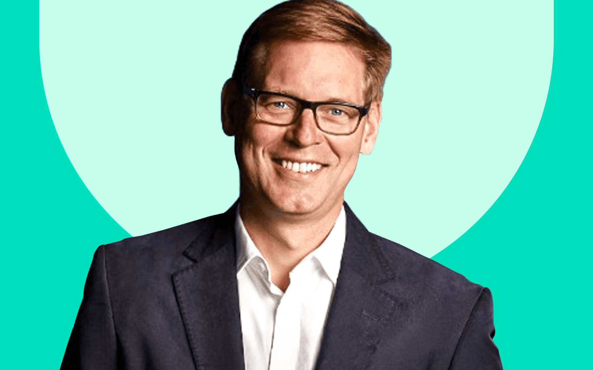 Smiling man in glasses, wearing a dark suit and white shirt, posed against a mint green background.