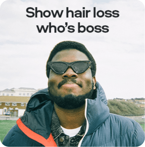 Man with sunglasses and a beard smiles outdoors. Text reads, "Sons. Show hair loss who's boss." Background shows houses and hills.