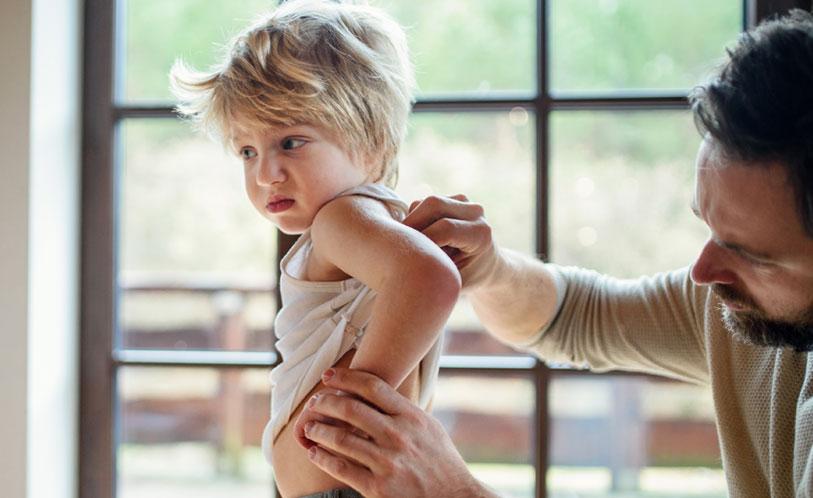 eczema image, male checking the skin on the back of a young boy