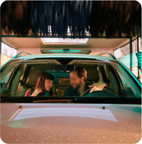 A man and woman smiling inside a car going through an automatic car wash, with water droplets on the windshield.